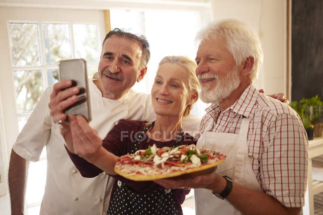Chef e casal sênior tomando selfie com pizza na aula de culinária — Fotografia de Stock
