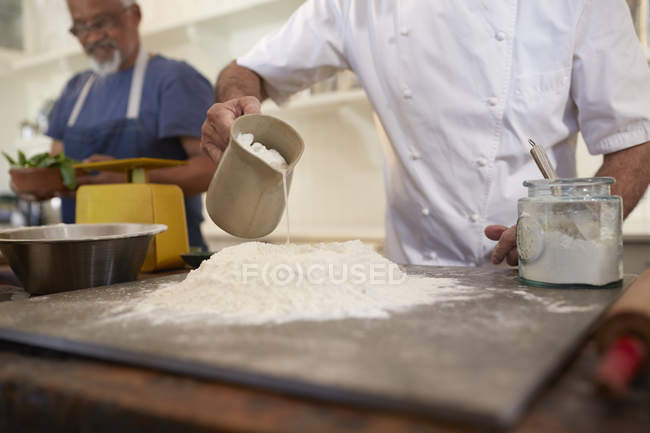 Primer plano chef verter agua en la masa de pizza nido de harina en la clase de cocina - foto de stock