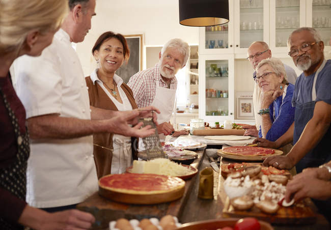 Старші друзі слухають шеф-кухаря в класі приготування піци — стокове фото