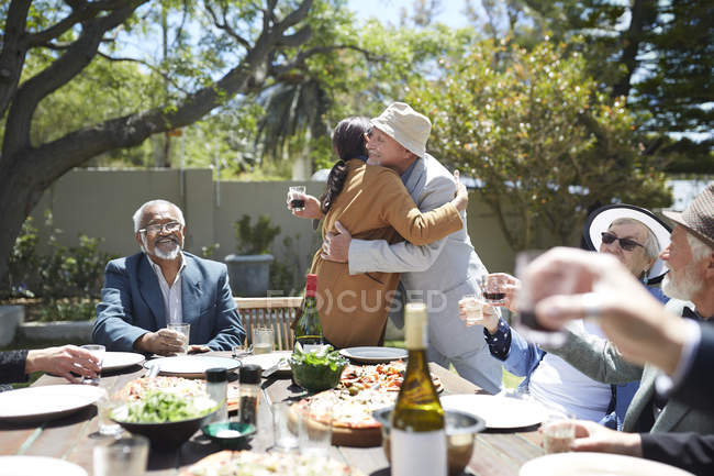 Amigos brindando cariñosa pareja de ancianos abrazándose en soleada fiesta en el jardín - foto de stock