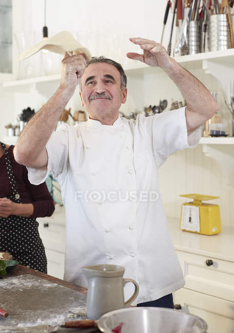 Playful senior chef tossing pizza dough in kitchen — Stock Photo