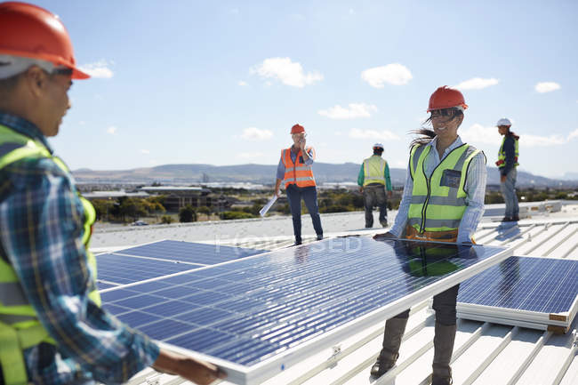 Ingenieros levantando panel solar en planta de energía soleada - foto de stock