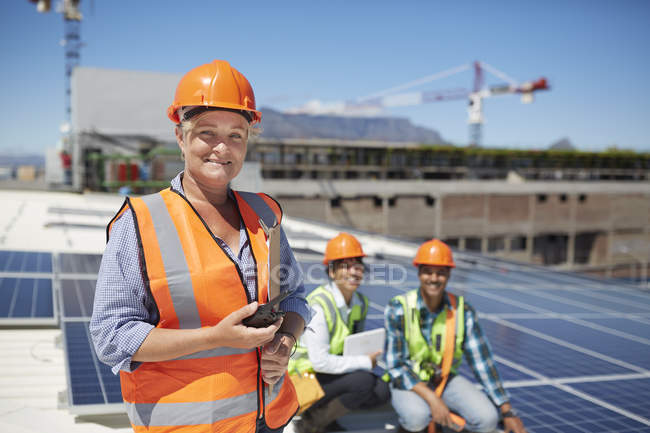 Retrato sorridente, engenheira feminina confiante com walkie-talkie na fábrica de energia solar ensolarada — Fotografia de Stock