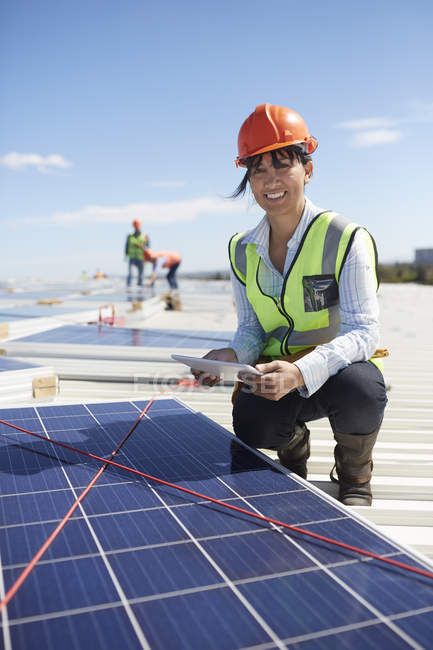 Portrait confident, smiling female engineer with digital tablet examining solar panels at power plant — Stock Photo