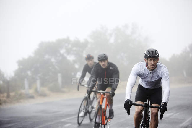 Ciclistas masculinos dedicados ciclismo en carretera lluviosa - foto de stock