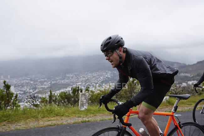 Ciclista masculino determinado en bicicleta por carretera lluviosa - foto de stock