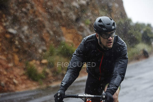 Присвячений молодий чоловік їде на велосипеді по дощовій дорозі — стокове фото