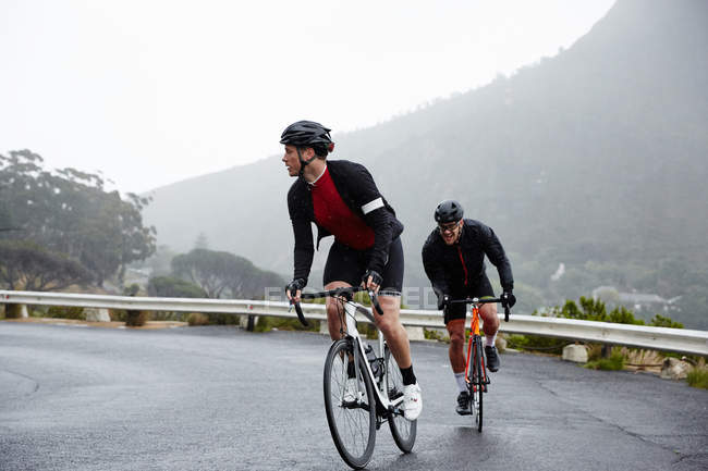 Присвячені чоловіки-велосипедисти на мокрій дорозі — стокове фото
