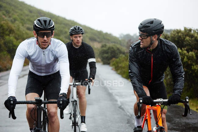 Ciclistas do sexo masculino ciclismo na estrada molhada — Fotografia de Stock