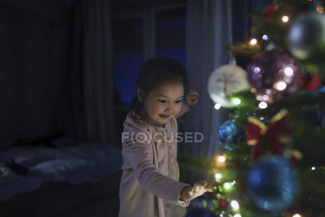 Curiosa, linda chica tocando el árbol de Navidad iluminado - foto de stock