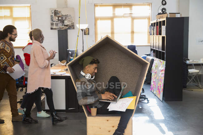 Hombre de negocios creativo con auriculares que trabajan en el ordenador portátil en cubículo - foto de stock