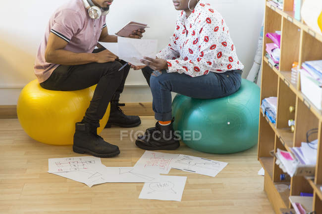 Креативні ділові люди зустрічаються, обговорюючи документи на фітнес-кулях в офісі — стокове фото