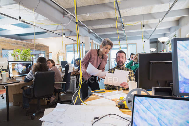 Творческие бизнесмены обсуждают бумажную работу в офисе открытого плана — стоковое фото