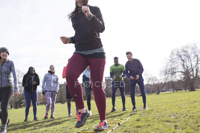 Team cheering woman doing speed ladder drill in sunny park — Stock Photo