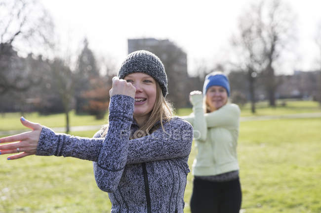 Smiling woman exercising, stretching arm in sunny park — Stock Photo
