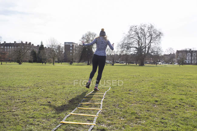 Donna che si allena, facendo il trapano a scala di velocità nel parco soleggiato — Foto stock