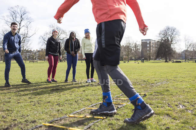Team watching man doing speed ladder drill in sunny park — Stock Photo