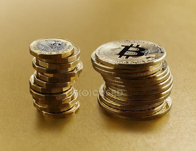 Bitcoins de oro apilados junto a monedas de libras británicas - foto de stock