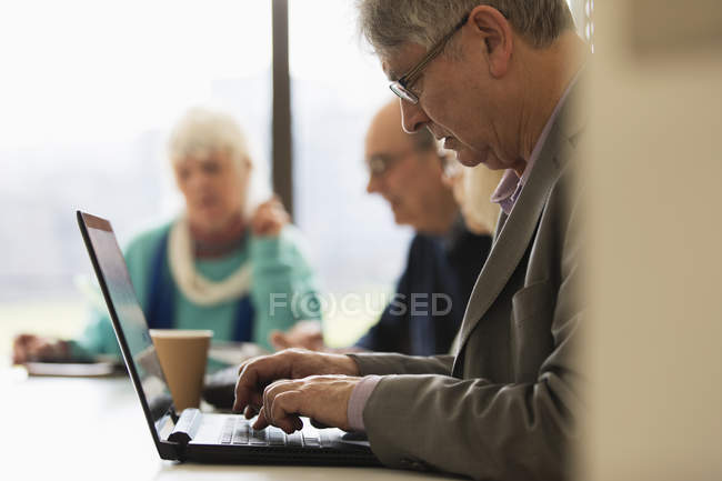 Uomo d'affari anziano concentrato che utilizza il computer portatile nella riunione della sala conferenze — Foto stock