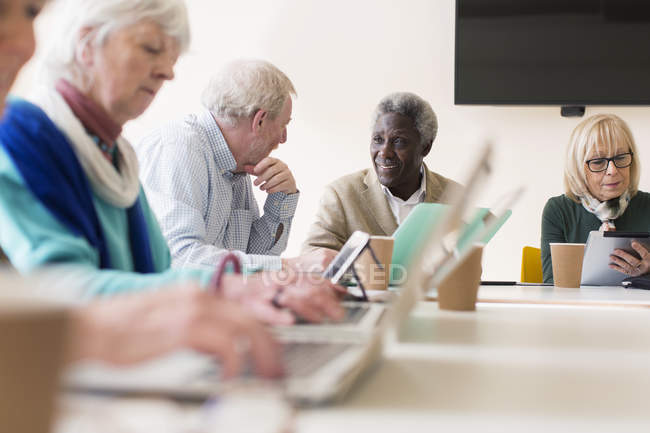 Старшие бизнесмены разговаривают, используют ноутбуки и цифровые планшеты в конференц-зале — стоковое фото