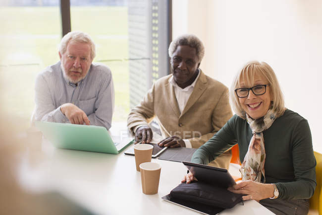 Des hommes d'affaires seniors souriants utilisant des tablettes numériques et un ordinateur portable lors d'une réunion en salle de conférence — Photo de stock