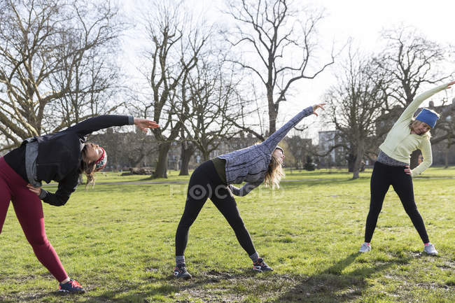 Women runners stretching in sunny park — Stock Photo