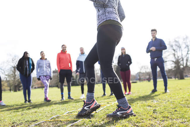 Team watching woman doing speed ladder drill in sunny park — Stock Photo