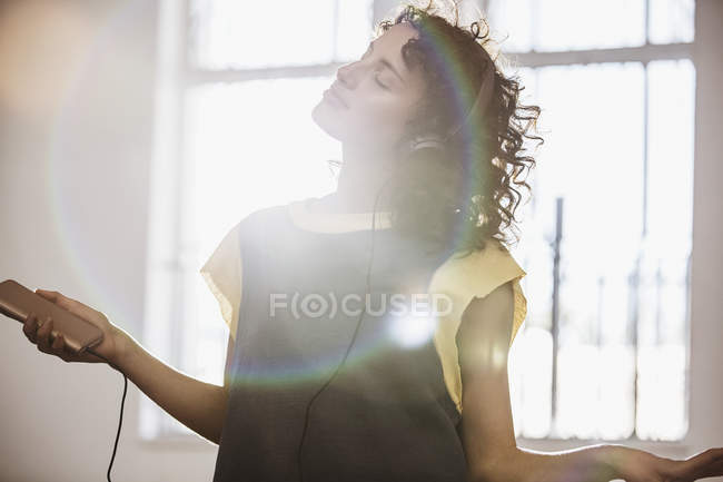 Безтурботний молода жінка-танцівниця слухає музику з навушниками та mp3 плеєром в сонячній студії — стокове фото