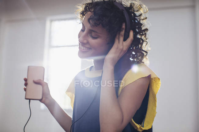 Усміхаючись, безтурботна молода жінка слухає музику з навушниками та mp3 плеєром — стокове фото