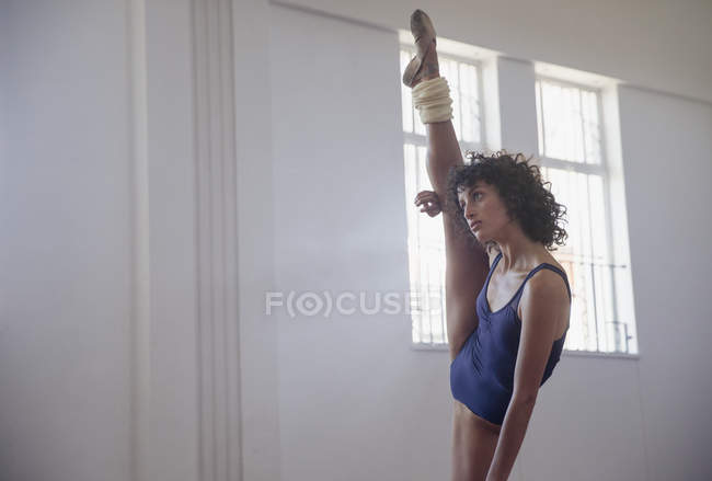 Flexible young female dancer stretching leg, doing standing splits in dance studio — Stock Photo
