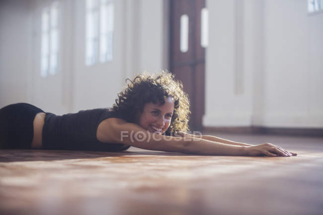 Lächelnde, unbeschwerte junge Tänzerin, die sich auf dem Boden des Tanzstudios dehnt — Stockfoto