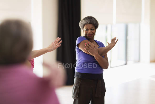 Smiling active senior stretching arm in exercise class — Stock Photo