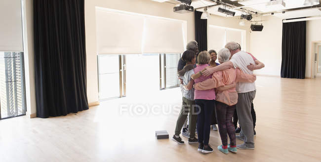 Ativo idosos ligação, abraçando em círculo no estúdio de exercícios — Fotografia de Stock