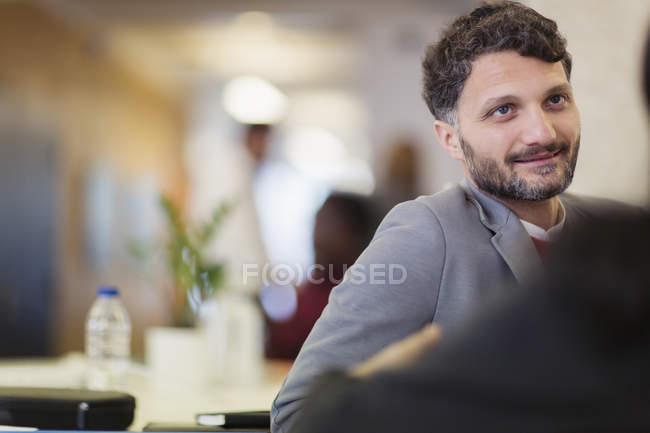 Улыбающийся бизнесмен слушает коллегу в офисе — стоковое фото