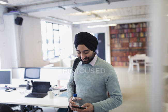 Empresario indio en turbante usando teléfono inteligente en la oficina - foto de stock