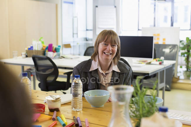 Retrato sonriente, empresaria confiada comiendo en la oficina - foto de stock