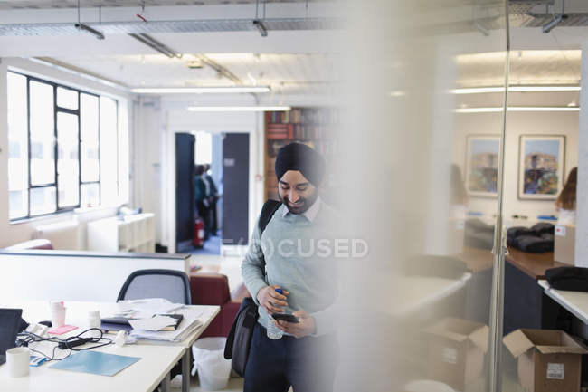 Индийский бизнесмен в тюрбане использует смартфон в офисе — стоковое фото