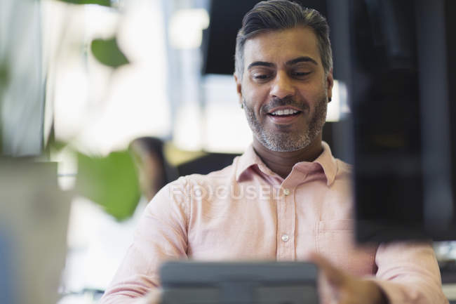 Hombre de negocios sonriente trabajando en la tableta digital en la oficina - foto de stock