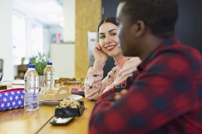 Mujer de negocios sonriente escuchando a hombre de negocios, almorzando en la oficina - foto de stock