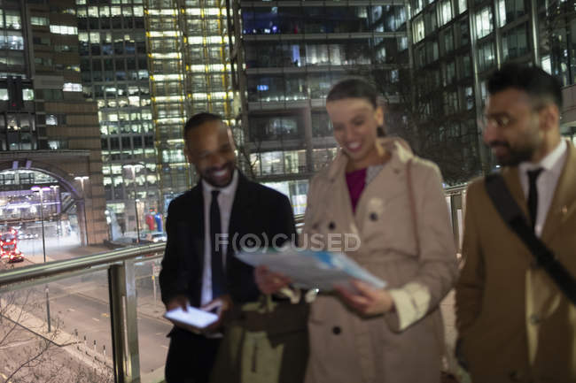 Gente de negocios revisando papeleo en puente peatonal urbano por la noche - foto de stock