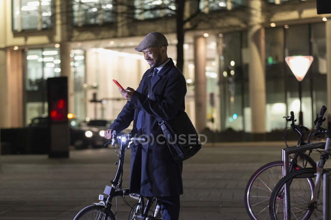Businessman with smart phone and bicycle on urban street at night — Stock Photo