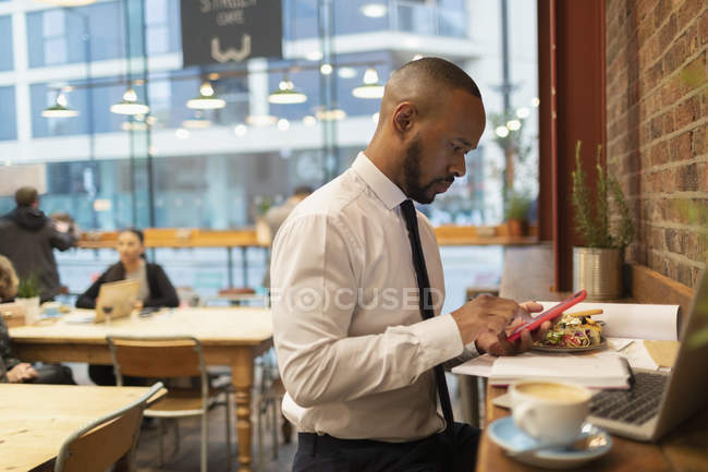 Businessman using smart phone and eating lunch in cafe — Stock Photo