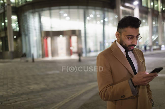 Бизнесмен переписывается со смартфоном на углу городской улицы ночью — стоковое фото