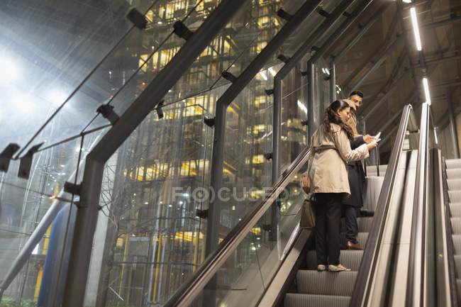 Gente de negocios con maleta hablando en escaleras mecánicas urbanas por la noche - foto de stock