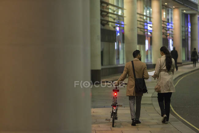Business people with bicycle walking on urban sidewalk at night — Stock Photo
