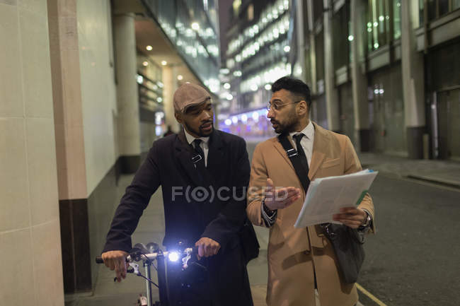 Empresarios con bicicleta y papeleo caminando por la acera urbana - foto de stock
