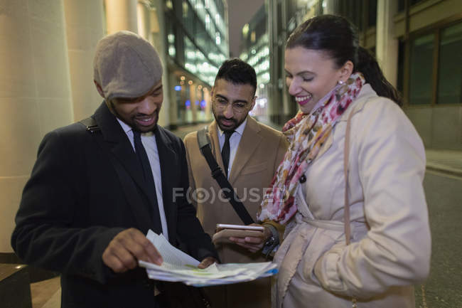 Business people reviewing paperwork on urban sidewalk at night — Stock Photo