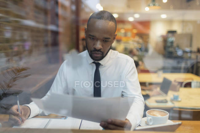 Фокусований бізнесмен розглядає документи, працюючи у вікні кафе — стокове фото