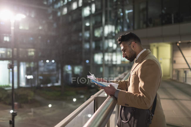 Businessman reviewing paperwork on urban pedestrian bridge at night — Stock Photo