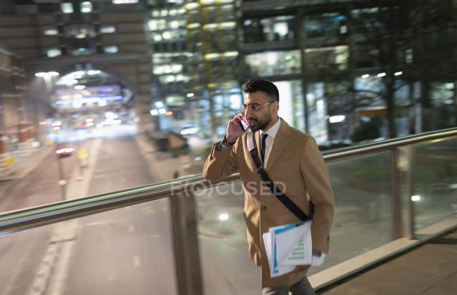 Uomo d'affari che parla di smart phone, cammina sul ponte pedonale urbano di notte — Foto stock